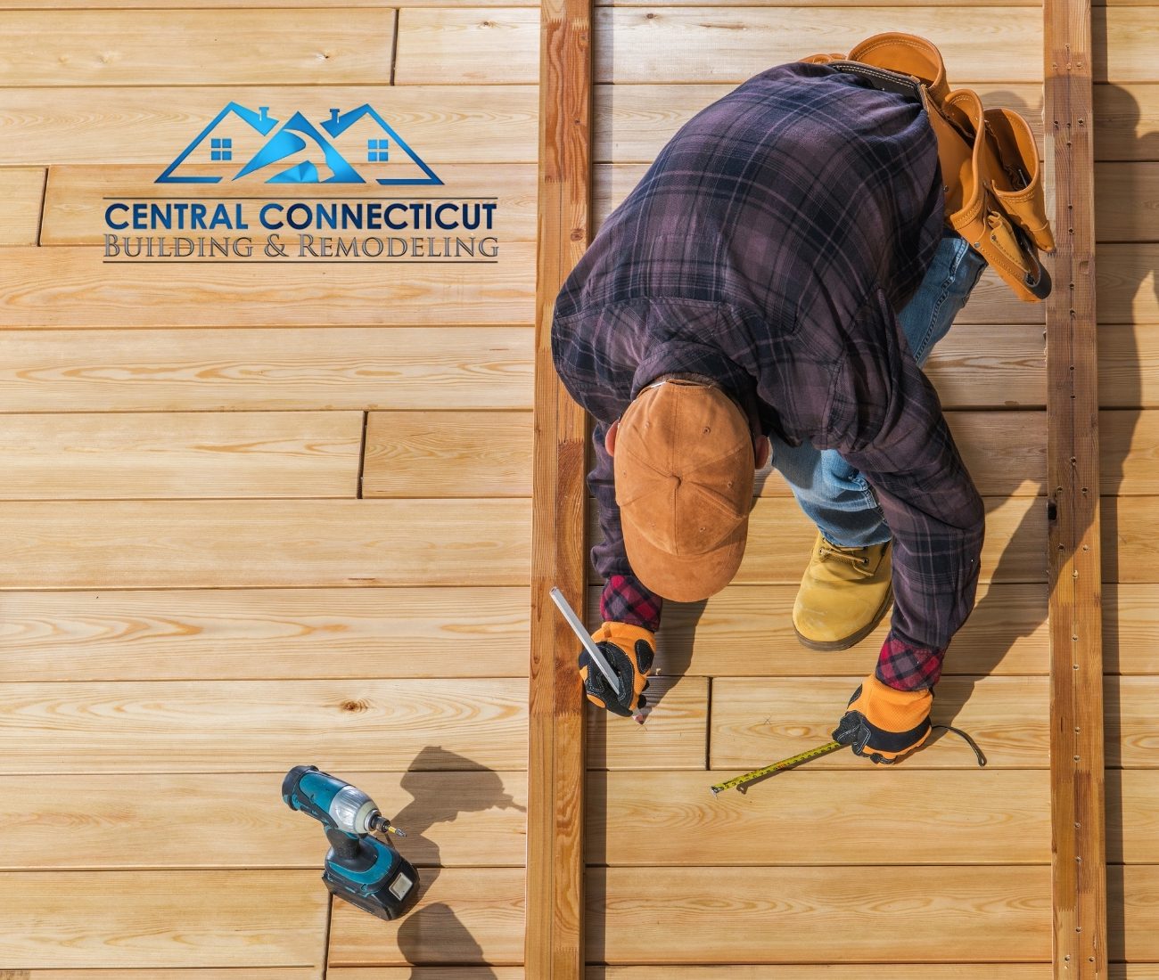 Overhead view of a deck builder marking measurements on freshly installed wood decking boards, wearing work gloves and a tool belt — Central Connecticut Building & Remodeling on site in Newington, CT.